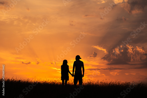 Silhouette of couple holding hands watching colorful sunset sky © Arthur Cauty