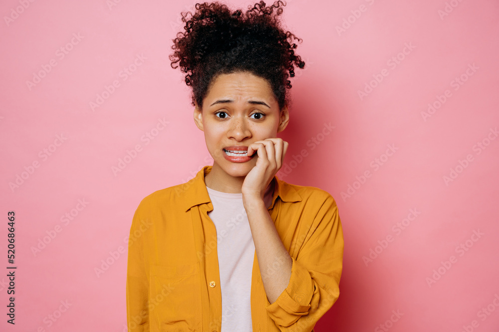 Confused worried african american young woman, in casual wear, looking stressed and nervous with hands on mouth biting nails, looking at camera, is going through, stands on isolated pink background Confused worried african american young woman, in casual wear, looking stressed and nervous with hands on mouth biting nails, looking at camera, is going through, stands on isolated pink background