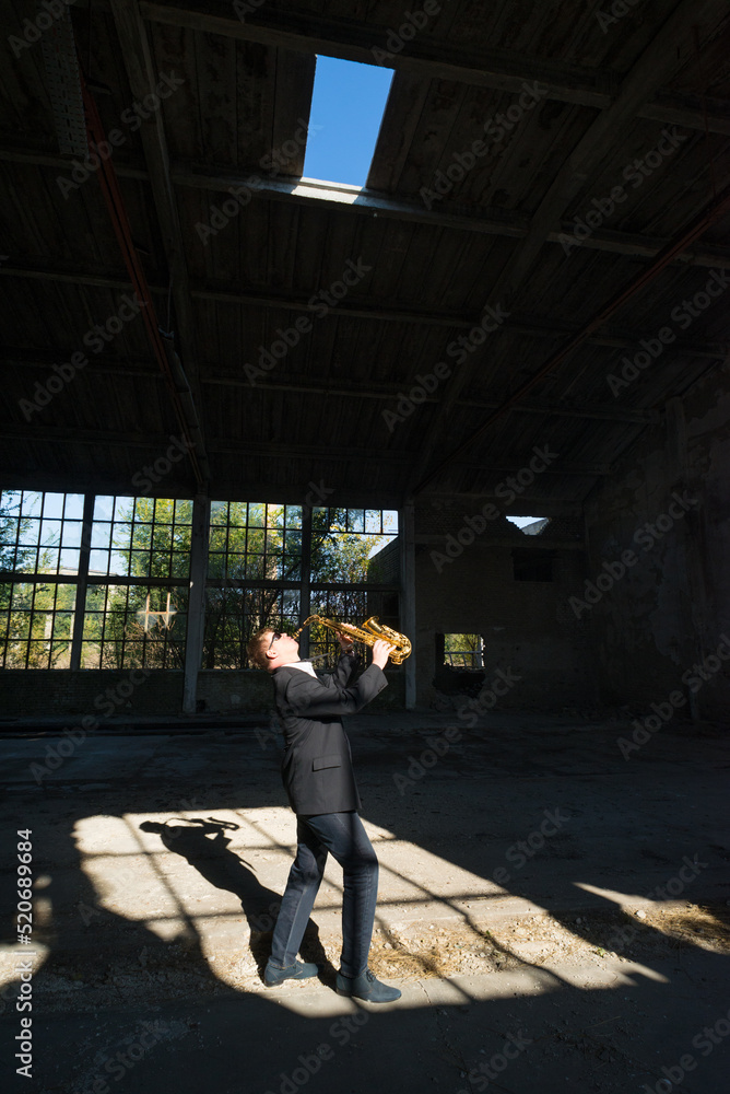 Man playing jazz on saxophone in the abandoned factory building on a sunny summer day Man playing jazz on saxophone in the abandoned factory building on a sunny summer day