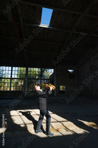 Man playing jazz on saxophone in the abandoned factory building on a sunny summer day
