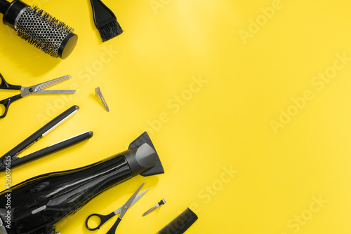 Scissors, hair dryer, hair straightener, combs, brush and hair clips lie on a yellow background photo