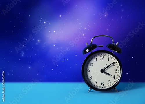 Alarm clock on turquoise table against night sky with stars, space for text. Insomnia