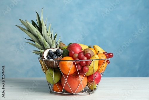 Fototapeta Naklejka Na Ścianę i Meble -  Assortment of fresh exotic fruits in metal basket on white wooden table against light blue background