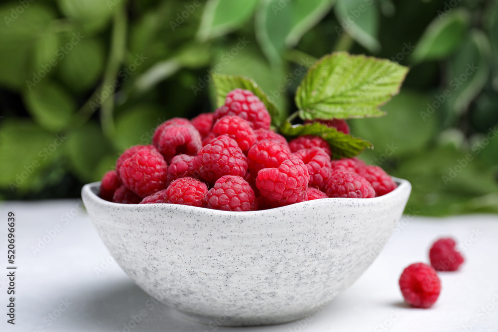 Bowl of fresh ripe raspberries with green leaves on white table against blurred background, closeup Bowl of fresh ripe raspberries with green leaves on white table against blurred background, closeup