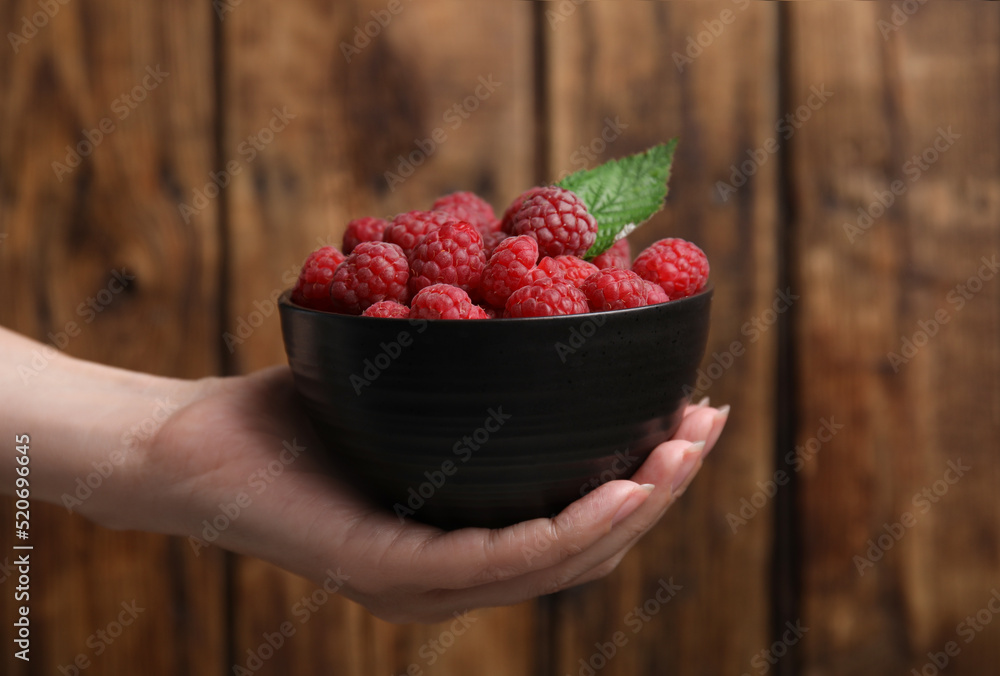Woman holding bowl with fresh ripe raspberries against wooden background, closeup - obrazy, fototapety, plakaty 