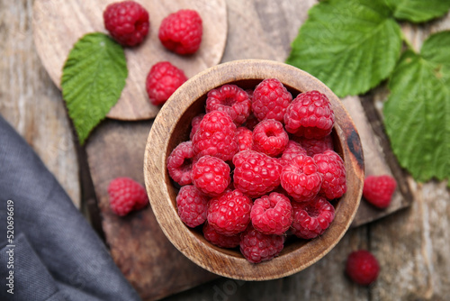 Bowl with fresh ripe raspberries and green leaves on wooden table, flat lay