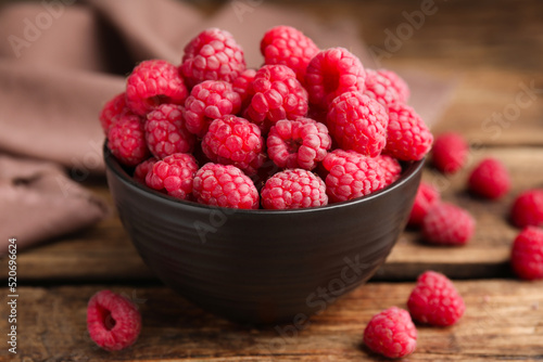 Bowl with fresh ripe raspberries on wooden table, closeup