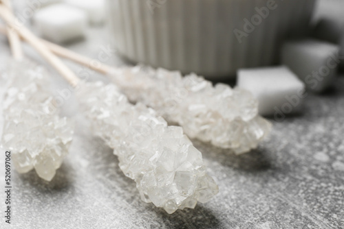 Sticks with sugar crystals on light grey table, closeup. Tasty rock candies