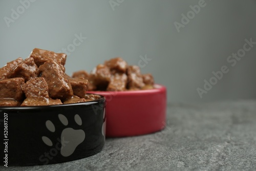 Wet pet food in feeding bowls on grey table, closeup. Space for text