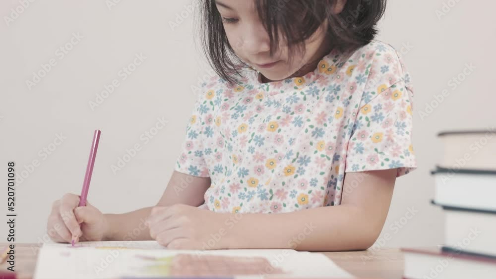 Adorable asian girl is doing her homework on the table with a lot of books and pencil. It shows concept of smart and clever child learning by herself to gain knowledge which is basic education. Adorable asian girl is doing her homework on the table with a lot of books and pencil. It shows concept of smart and clever child learning by herself to gain knowledge which is basic education.