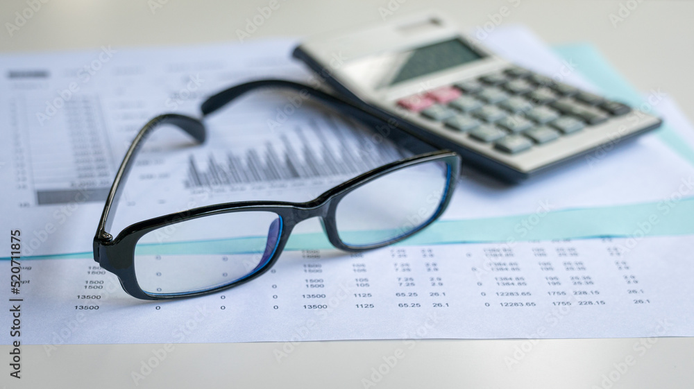Eyeglasses and calculator on top of financial report and charts. Financial accounting and market trends concept. Eyeglasses and calculator on top of financial report and charts. Financial accounting and market trends concept.