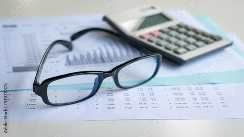 Eyeglasses and calculator on top of financial report and charts. Financial accounting and market trends concept.