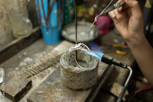 Close-up of a hand of a goldsmith who builds a precious jewel with silver. To make the jewel it takes: precision, craftsmanship and patience. Concept: silver, style, production.