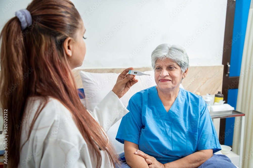 Obraz premium Indian doctor check fever of old senior female patient using thermometer at hospital or clinic. Elderly people health care concept.