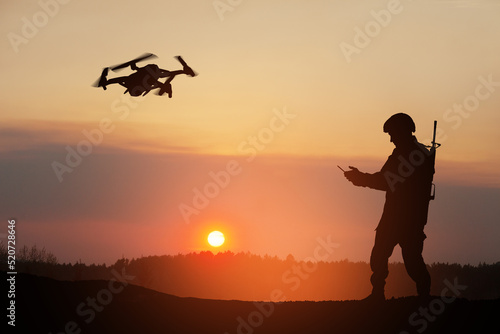 Silhouette of soldier are using drone and laptop computer for scouting during military operation against the backdrop of a sunset. Greeting card for Veterans Day  Memorial Day  Independence Day.