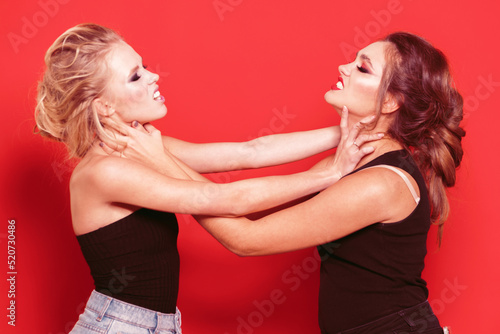 Two pretty girls fighting in the studio. Red background. photo