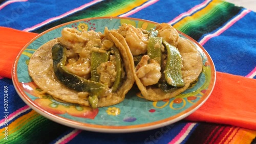 Two tacos gobernador sit on a colorful plate over vivid Mexican tablecloths. The ingredients of these iconic tacos of Sinaloa, Mexico, include shrimp, cheese and roasted poblano peppers. photo