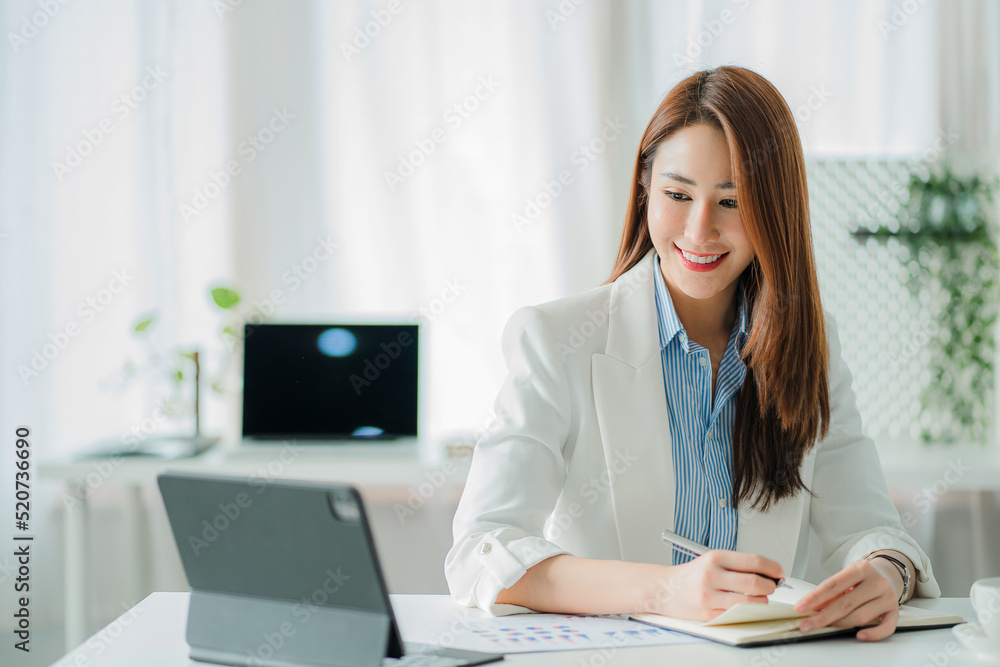 Beautiful smiling Asian businesswoman working using a tablet at the office while sitting in a modern office successful business idea Beautiful smiling Asian businesswoman working using a tablet at the office while sitting in a modern office successful business idea