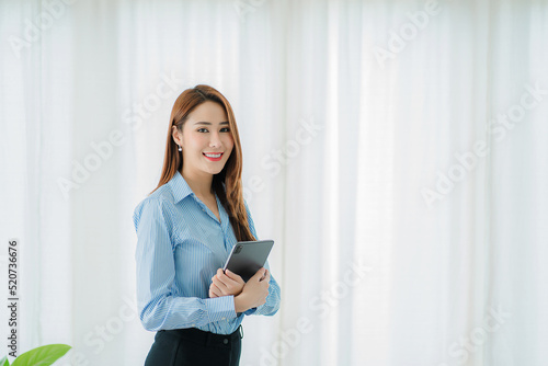 Free Download Asian professional businesswoman holding a tablet standing by a glass plate window in the office - GFXLoad
