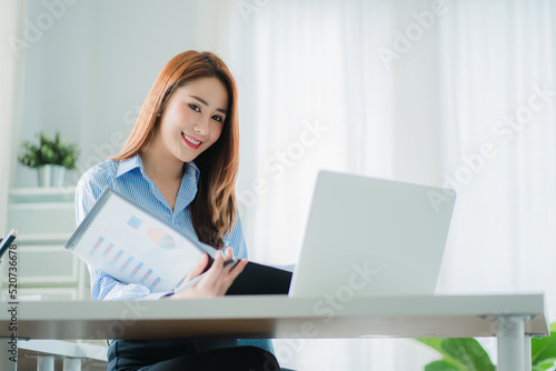 Professional and intelligent Asian businesswoman or female financial analyst working on her financial reports. Analyze graphs and charts with a laptop.