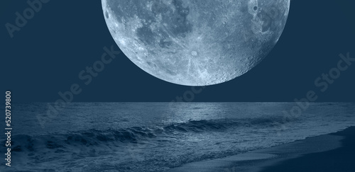 Night sky with blue moon in the clouds over the calm blue sea 