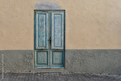 Exterior of an old house with a light blue weathered door on grey and yellow wall, Tuscany, Italy