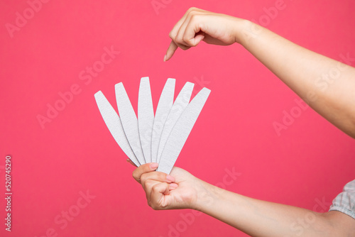Set of nail files in woman hand and points to one of them on pink background. Manicurist equipment photo