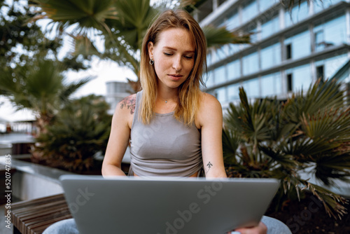 Young beautiful casual woman working on a laptop sitting on the bench in the street © fotofabrika