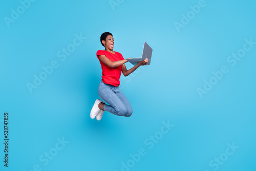Photo of good mood pretty short hair human wear red t-shirt jumping high typing modern device isolated blue color background