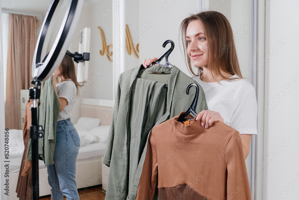 Female Blogger Recording Vlog Video on smartphone At Home Online Influencer On near wardrobe choosing clothes, earthly look. Stylist on-line consulting Dress or shirt. Female Blogger Recording Vlog Video on smartphone At Home Online Influencer On near wardrobe choosing clothes, earthly look. Stylist on-line consulting Dress or shirt.