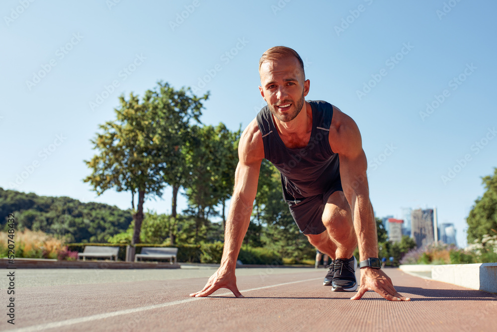 Young handsome man in a starting position for running on a sports track.