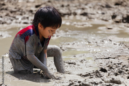 cute happy asian little boy enjoying to play in the mud at playground. child learning in nature at montessori school. nature and education concept.