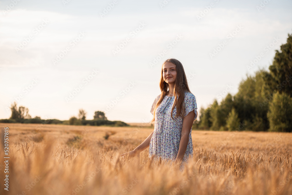 Happy smiling girl in white dress looking to the camera. Beautiful teenage girl walking in field of ripe wheat Happy smiling girl in white dress looking to the camera. Beautiful teenage girl walking in field of ripe wheat