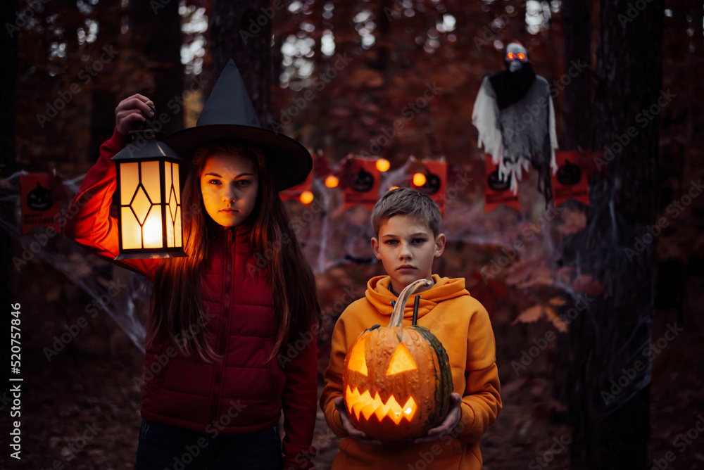 Fototapeta premium Little girl and boy with halloween decorations in Autumn forest. Halloween celebration, spooky atmosphere