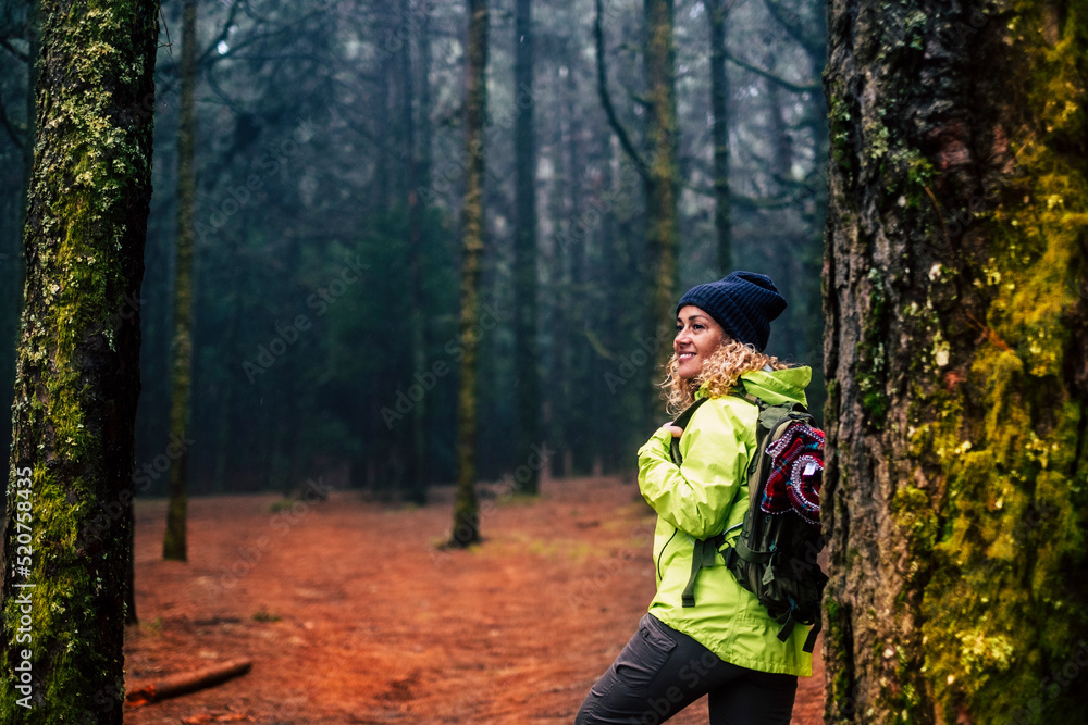 Happy female excursionist enjoy nature background and forest around smiling and resting against a tree. Travel backpacker woman in outdoor leisure activity alone. Alternative tourism lifestyle