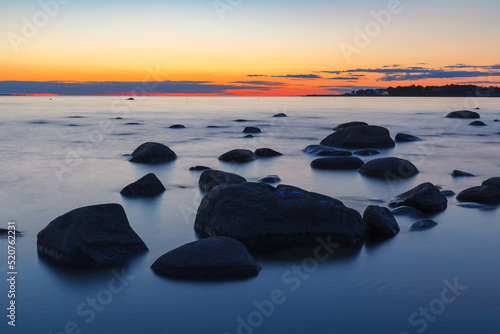 Rocky shore with stones sinking in the sea water. Sunset, long exposure. Baltic sea