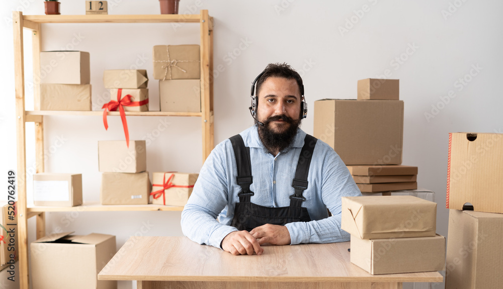 Start up. young man small business owner working at home office using headphones looking at camera. SME e-commerce telemarketing Start up. young man small business owner working at home office using headphones looking at camera. SME e-commerce telemarketing