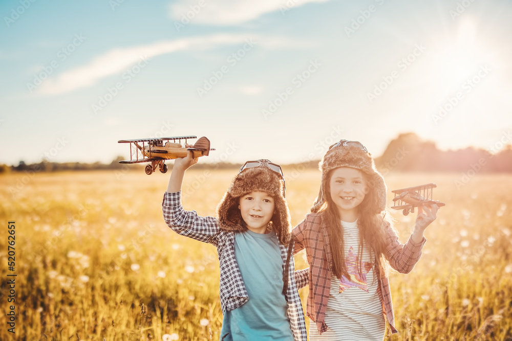 Boy and girl plaing with wooden planes on the field in sunset - obrazy, fototapety, plakaty 
