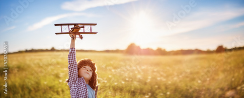 Fotografia Boy plaing with retro wooden plane on the field in sunset