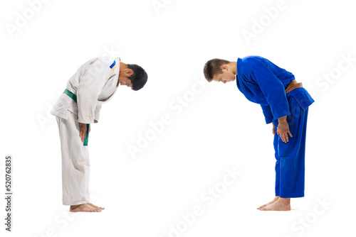 Portrait of two young men, martial arts sportsmen greeting, bowing isolated over white background
