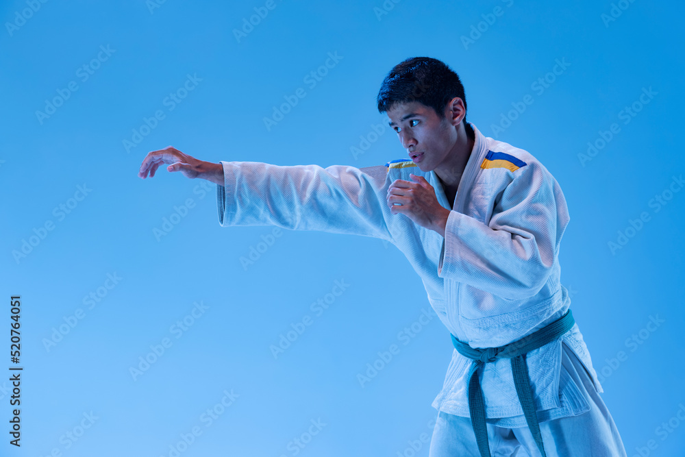 Portrait of young sportive man posing, training punch exercises isolated over blue studio background in neon light Portrait of young sportive man posing, training punch exercises isolated over blue studio background in neon light