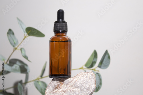 Fototapeta Naklejka Na Ścianę i Meble -  Cosmetic bottle serum, oil on stone stand with branch eucalyptus on grey background. Natural cosmetics concept, skin care product. Beauty concept for face body care