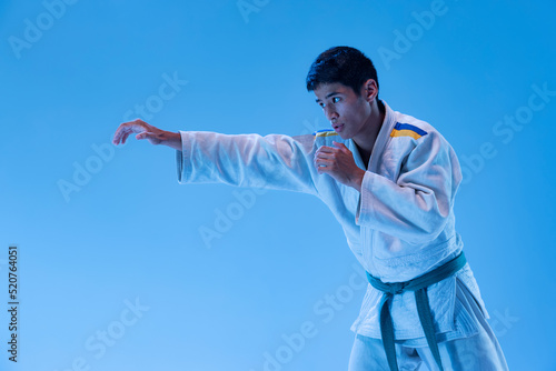 Portrait of young sportive man posing, training punch exercises isolated over blue studio background in neon light