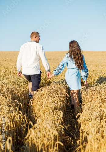 A couple in embroidered dresses are walking in a wheat field holding each other's hands