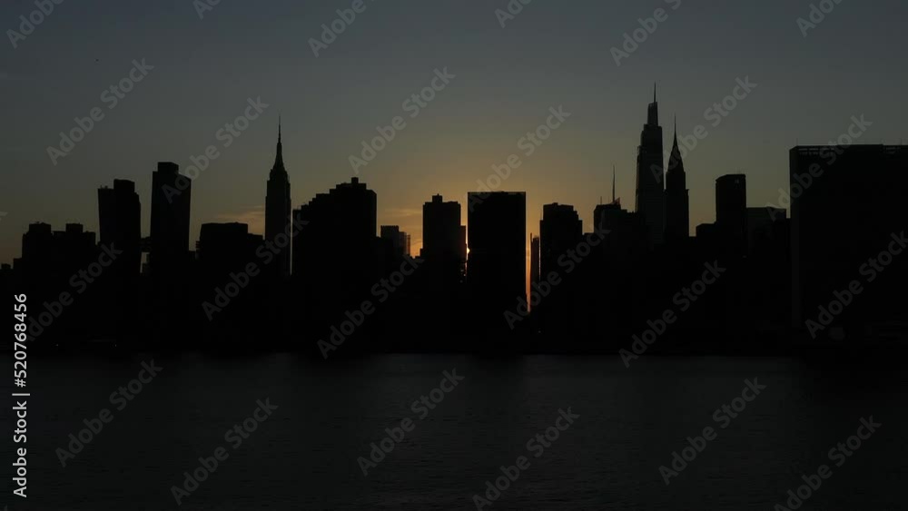 slow trucking shot of a silhouetted Manhattan skyline at sunset, just after the rare Manhattanhenge, a small sunbeam creeps from between the buildings slow trucking shot of a silhouetted Manhattan skyline at sunset, just after the rare Manhattanhenge, a small sunbeam creeps from between the buildings
