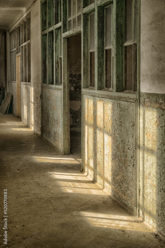Lost place hallway in an old barracks with door and broken windows and peeling wall paint in pastel colors and light through windows with window crosses Lost place hallway in an old barracks with door and broken windows and peeling wall paint in pastel colors and light through windows with window crosses