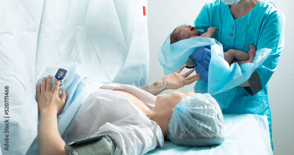 Nurse holds newborn baby close to mother in hospital Nurse holds newborn baby close to mother in hospital