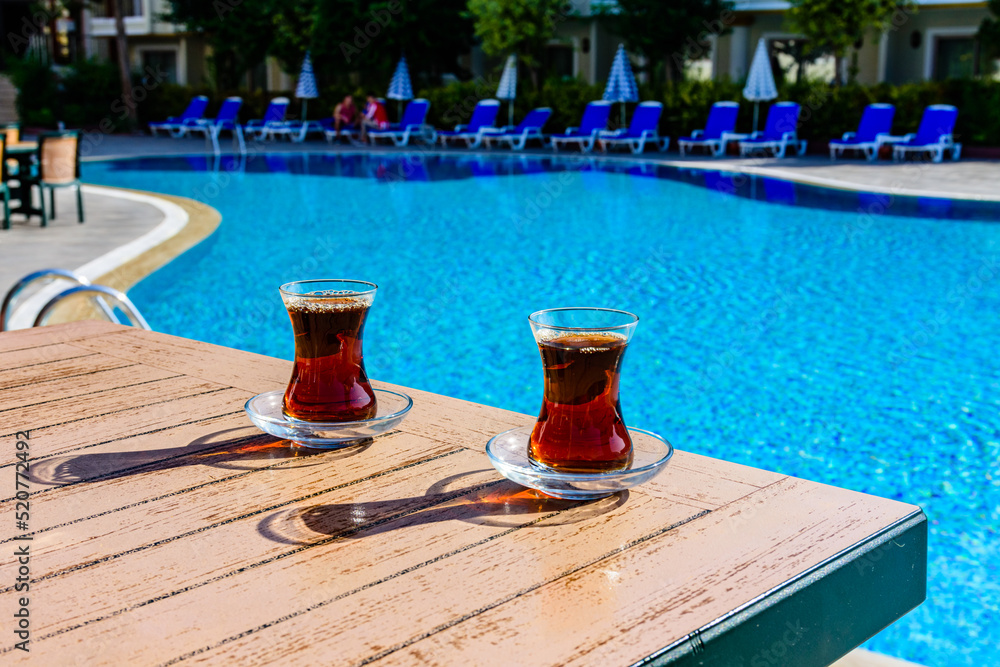 Black tea in traditional turkish glasses on table near the swimming pool Black tea in traditional turkish glasses on table near the swimming pool