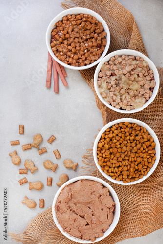 Different types of cat food in bowls with burlap material on grey surface with copy space