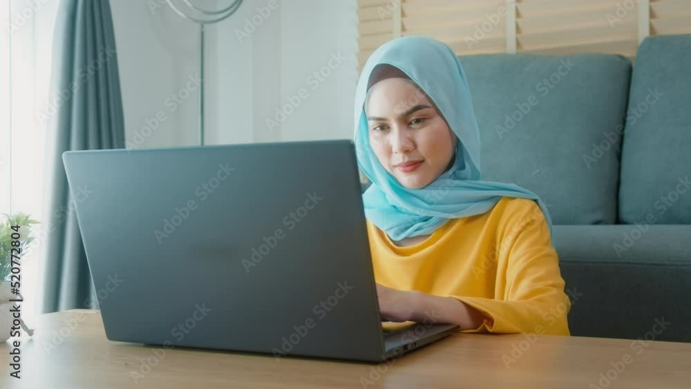Young happy muslim woman working on laptop in living room at home. Young happy muslim woman working on laptop in living room at home.